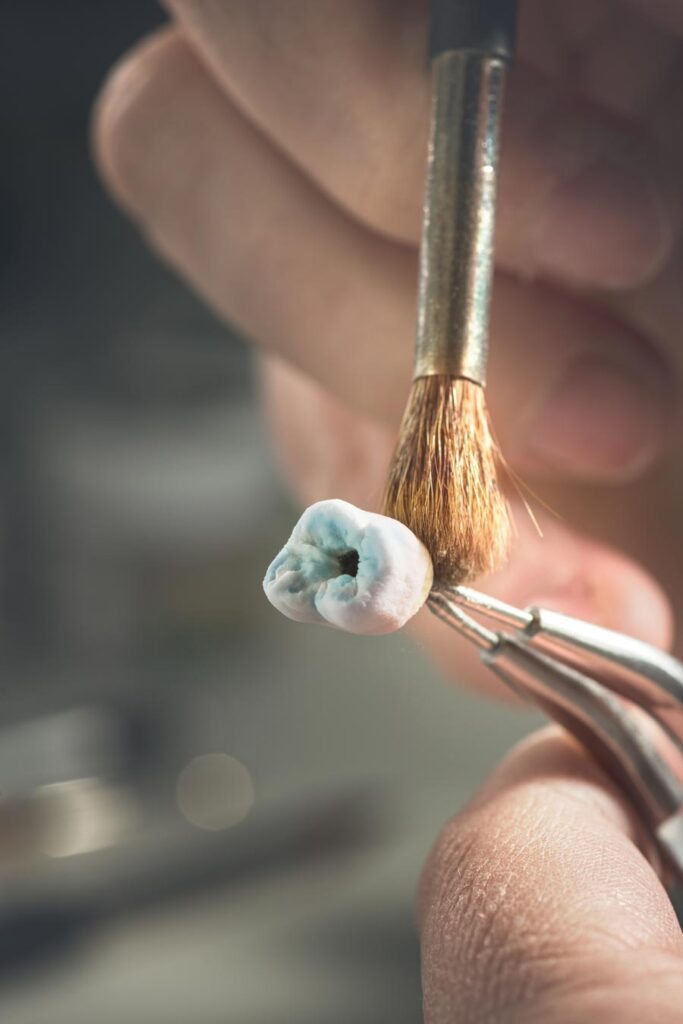 Dental technician sculpting tooth model with brush.